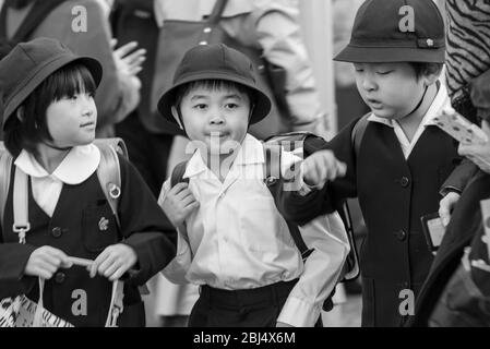 Tre bambini giapponesi con uniformi scolastiche che camminano lungo la strada trafficata accanto al mercato di Ameyoko a Tokyo, Giappone Foto Stock