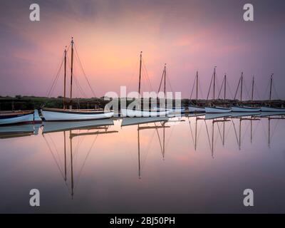 Una linea di identici e barche a vela all'alba in una tranquilla mattina di primavera. Foto Stock