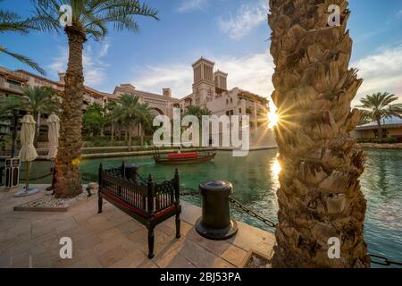 Il sole si tramonta in raggi brillanti mentre un abra passa nel suk Madinat Jumeirah a Dubai. Foto Stock