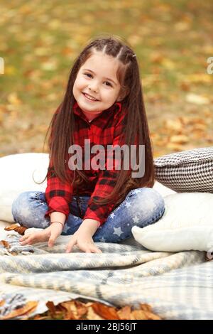 Felice ragazza giovane seduta su plaid in autunno parco Foto Stock