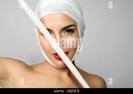 Giovane bella donna che chiude il viso con garza, su sfondo grigio Foto Stock