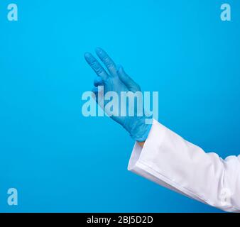 medic in un cappotto bianco, guanti blu in lattice tira la mano su uno sfondo blu Foto Stock