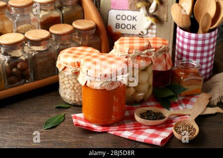 Vasetti con verdure e fagioli sottaceto, spezie, libro di ricette e utensili da cucina su sfondo legno Foto Stock