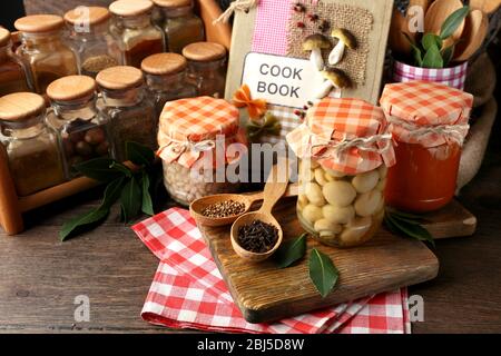 Vasetti con verdure e fagioli sottaceto, spezie, libro di ricette e utensili da cucina su sfondo legno Foto Stock