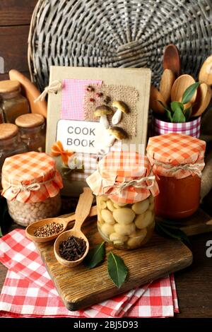 Vasetti con verdure e fagioli sottaceto, spezie, libro di ricette e utensili da cucina su sfondo legno Foto Stock