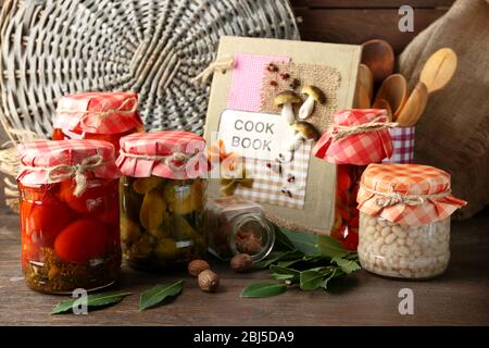 Vasetti con verdure e fagioli sottaceto, spezie, libro di ricette e utensili da cucina su sfondo legno Foto Stock
