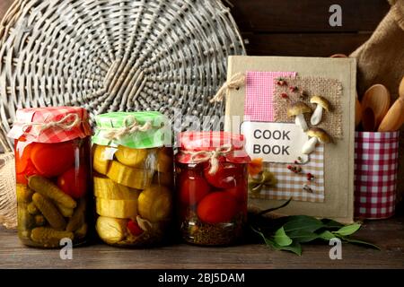 Vasetti con verdure e fagioli sottaceto, spezie, libro di ricette e utensili da cucina su sfondo legno Foto Stock