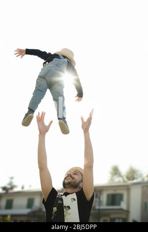 Stare a casa: Un padre e il suo figlio giocano insieme nel cortile: L'uomo getta il bambino in aria. Foto Stock