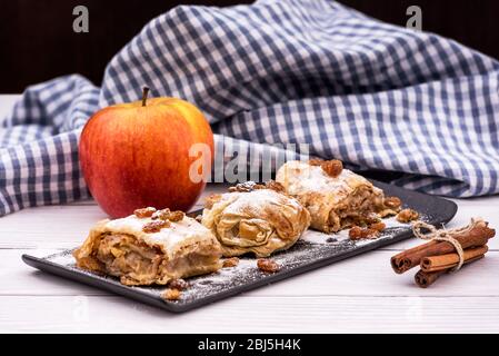 Fette di strudel di torta di mele fatta in casa in un piatto con ingredienti su un rustico tavolo di legno bianco. Torta con mele, uvetta e cannella, dolci Foto Stock