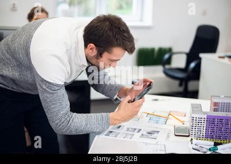 Un giovane architetto che fotografa il modello di costruzione mentre era in ufficio. Foto Stock