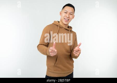un uomo asiatico sicuro con felpa con cappuccio marrone mostra le mani come su sfondo bianco. Foto Stock