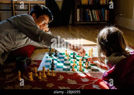 Un papà sorridente si trova a terra con la bambina che gioca scacchi al sole Foto Stock