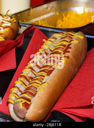 Concetto di cibo di strada, hot dog con salse in mostra sul tovagliolo rosso Foto Stock