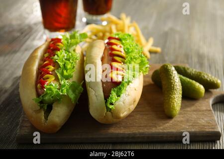 Deliziosi hot-dog con cetrioli sottaceto su tagliere di legno Foto Stock