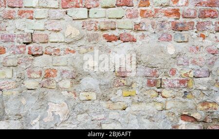 Sfondo di vecchio muro di mattoni parzialmente coperto da calcestruzzo. Foto Stock