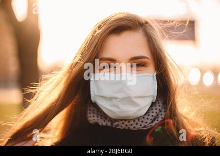 Ritratto di giovane donna felice che indossa maschera protettiva viso medico in piedi in città al tramonto Foto Stock