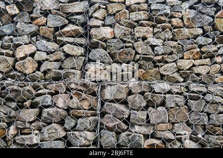 sfondo - parete gabionica di rete esagonale con massi in granito Foto Stock