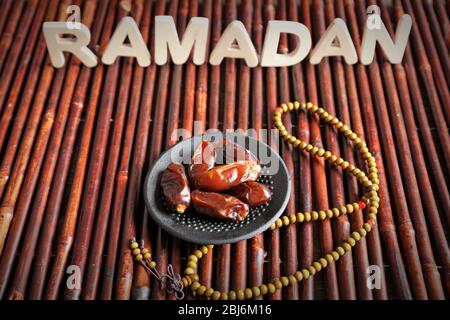 Immagine della parola RAMADAN con rosario e datteri frutta su sfondo legno, primo piano Foto Stock