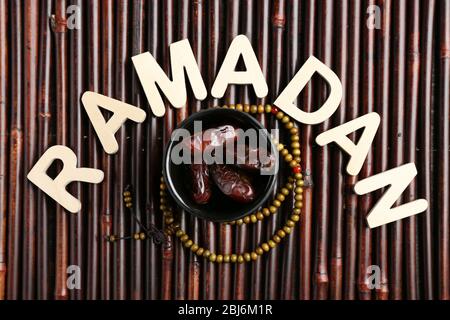 Immagine della parola RAMADAN con rosario e datteri frutta su sfondo legno, primo piano Foto Stock