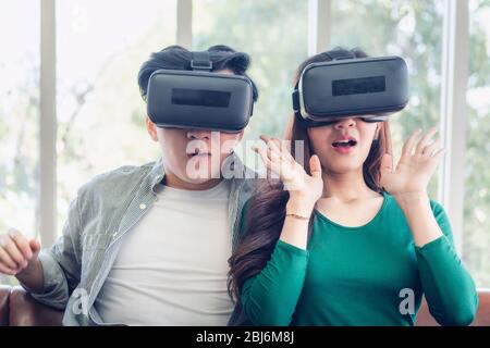 Giovane coppia divertirsi guardando video attraverso la realtà virtuale insieme. Coppia ama divertirsi con gli occhiali elettronici VR Gaming on Couch. IT Foto Stock
