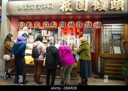 Gli amanti dello shopping nel quartiere di Gion, sulla via principale di Shijo-dori, scelgono un cibo di strada da acquistare. Foto Stock