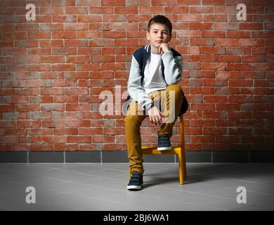Carino ragazzo seduto su una sedia vicino a muro di mattoni Foto Stock