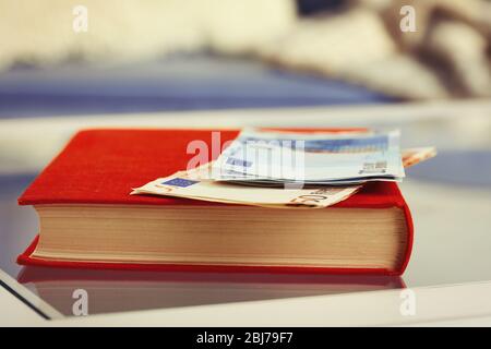 Libro rosso con banconote in euro su un tavolo di vetro Foto Stock