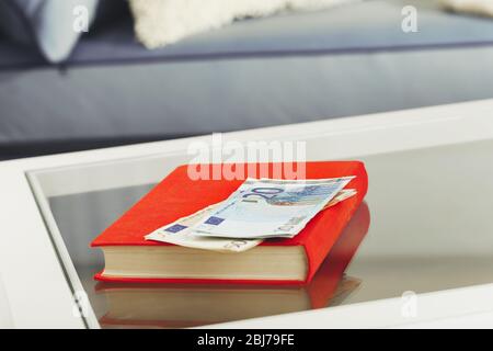 Libro rosso con banconote in euro su un tavolo di vetro Foto Stock