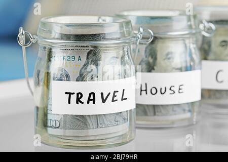 Vasi di vetro con banconote in dollari per la casa e viaggi su un tavolo Foto Stock