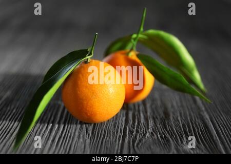 Tangerini freschi con foglie su tavola di legno, primo piano Foto Stock