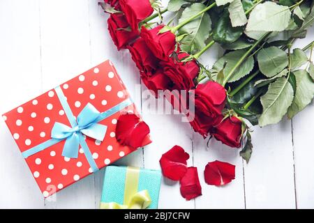 Bel bouquet di rose rosse e scatole presenti su sfondo di legno Foto Stock