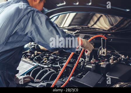 Autofficine fermo batteria energia elettrica attraverso i cavi ponticello e controllo al veicolo di manutenzione da parte del cliente secondo la rivendicazione ordine nel negozio di riparazioni auto in garage. Foto Stock