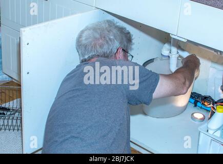 uomo anziano che fissa un tubo che perde sotto il lavandino Foto Stock