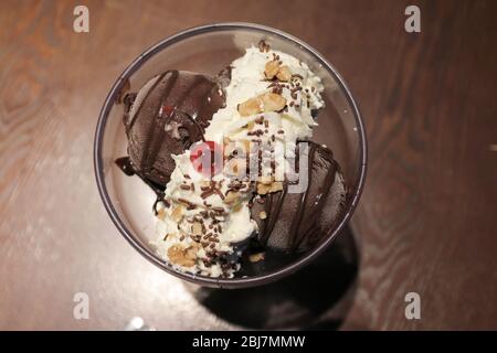 Immagine dall'alto del gelato al cioccolato in una ciotola con panna montata e ciliegia sulla parte superiore Foto Stock