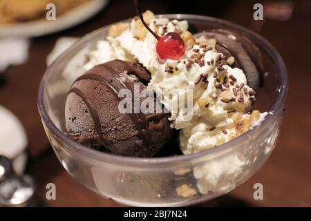 Gelato al cioccolato in una ciotola con panna da montare e ciliegia sulla parte superiore. Foto Stock