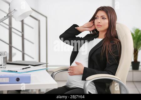Donna incinta seduta sul suo posto di lavoro in ufficio Foto Stock