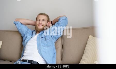 Sorridente rilassato giovane uomo chill su comodo coulhc guardando lontano. Foto Stock