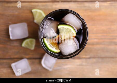 Cocktail con fette di lime e blocchi di ghiaccio su tavolo di legno, vista dall'alto Foto Stock