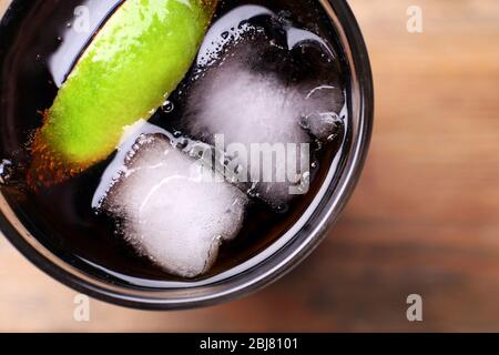 Cocktail con fette di lime e blocchi di ghiaccio su tavolo di legno, primo piano Foto Stock