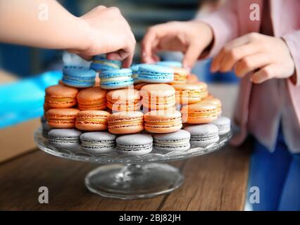 Mani femminili che prendono gustosi macaroon dal piatto sul tavolo Foto Stock