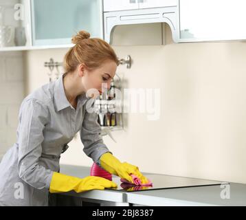 Giovane donna che pulisce una stufa elettrica con un panno e detergente Foto Stock