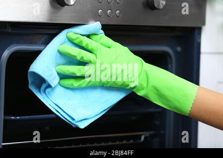 Donna mano in guanto protettivo forno di pulizia con straccio Foto Stock