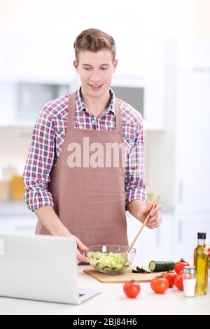 Uomo bello cucinare insalata di verdure in cucina Foto Stock