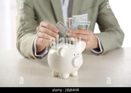 Uomo che mette i soldi in una banca di pigy a tavola di legno closeup Foto Stock