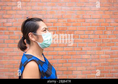 Donne asiatiche che indossano una maschera sfondo muro di mattoni. Foto Stock