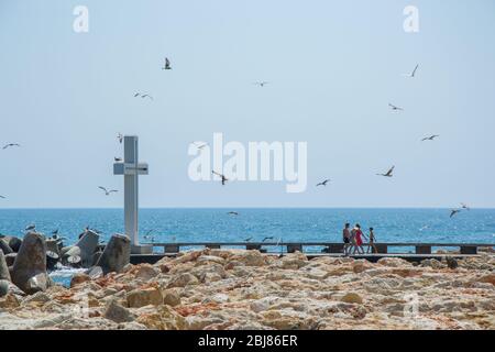 Mare, vista di una grande croce di cemento sulla baia, persone a piedi e uccelli volare, acque blu e cielo, frangiflutti, stagione estiva, natura Foto Stock