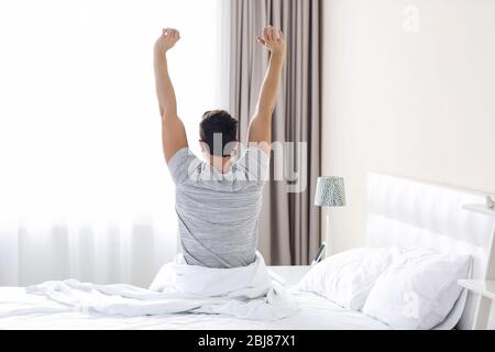 Un giovane uomo di svegliarsi nel letto e stirando le braccia Foto Stock