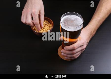 Mano maschile che tiene un bicchiere di birra su sfondo scuro Foto Stock