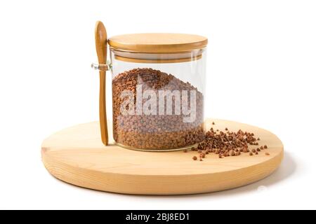 Grani di grano saraceno marrone in vaso di vetro con cucchiaio di legno e coperchio su sfondo bianco isolato cibo sano, concetto di superfood. Foto Stock