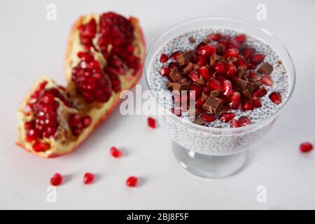 Budino di semi di Chia con granelli di melograno e patatine di cioccolato in piattino di vetro su fondo bianco Foto Stock